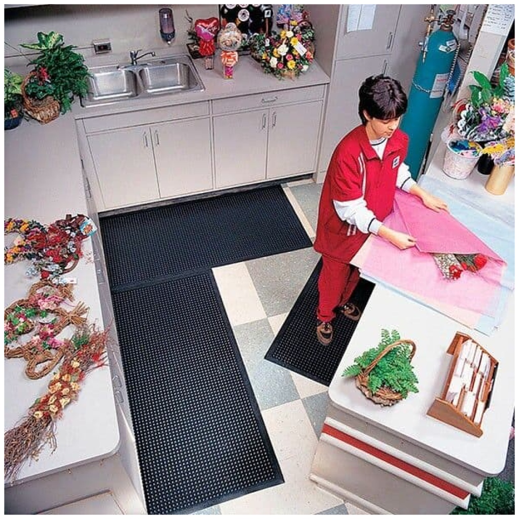 A boy in a red shirt is standing on a Comfort-Eze Floor Mat in a kitchen.