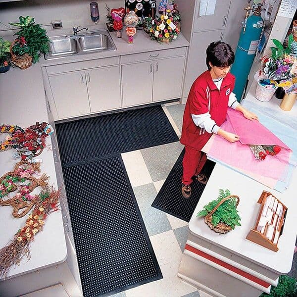 A boy in a red shirt is standing on a Comfort-Eze Floor Mat in a kitchen.