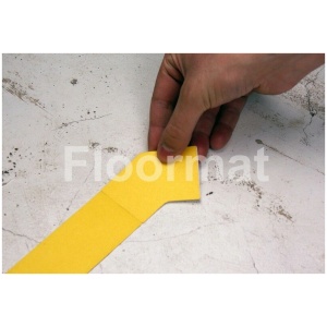 A person using a 45 Degree Corners Pallet Floor Markers to cut a corner of yellow tape marking the floor.