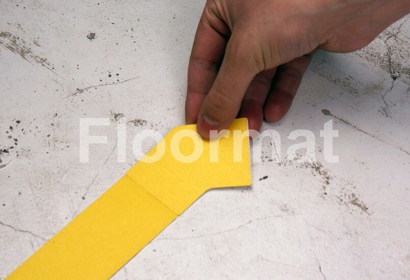 A person using a 45 Degree Corners Pallet Floor Markers to cut a corner of yellow tape marking the floor.