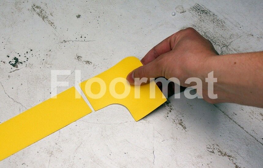 A person cutting a yellow tape on a white floor marked with 90 Degree Corners Pallet Floor Markers.