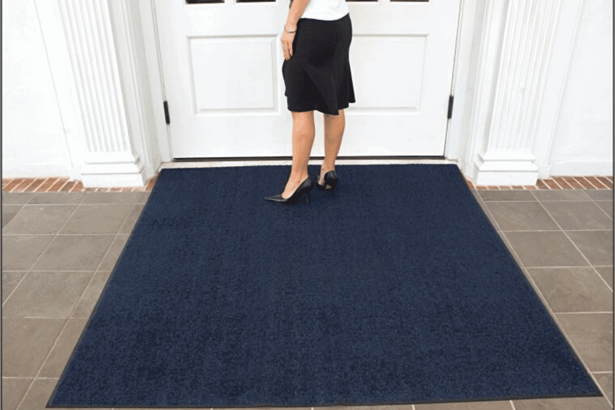 A woman standing in front of a door with a blue door mat.