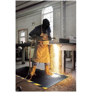 A man is welding on a DuraComfort Grip Floor Mat in a factory.