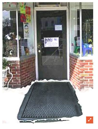 A black mat in front of a store with snow on it.