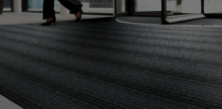 A person walking down a hallway with an anti-slip black carpet mat.