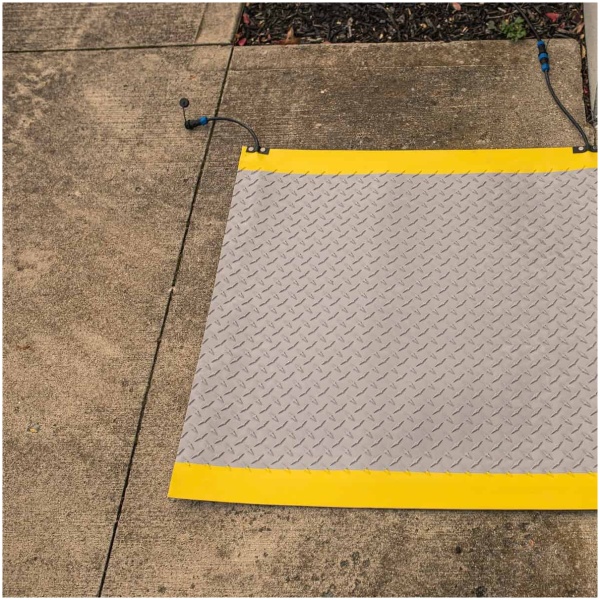 A yellow ProHeat Snow Melting Floor Mat on the sidewalk next to a door.