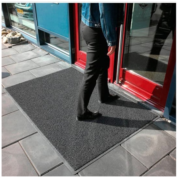A person walking on a black mat in front of a building.