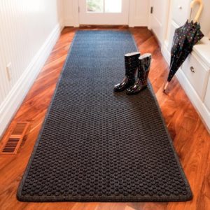 A black runner rug in a hallway with rain boots, teaching homeowners how to stop dirt from entering.