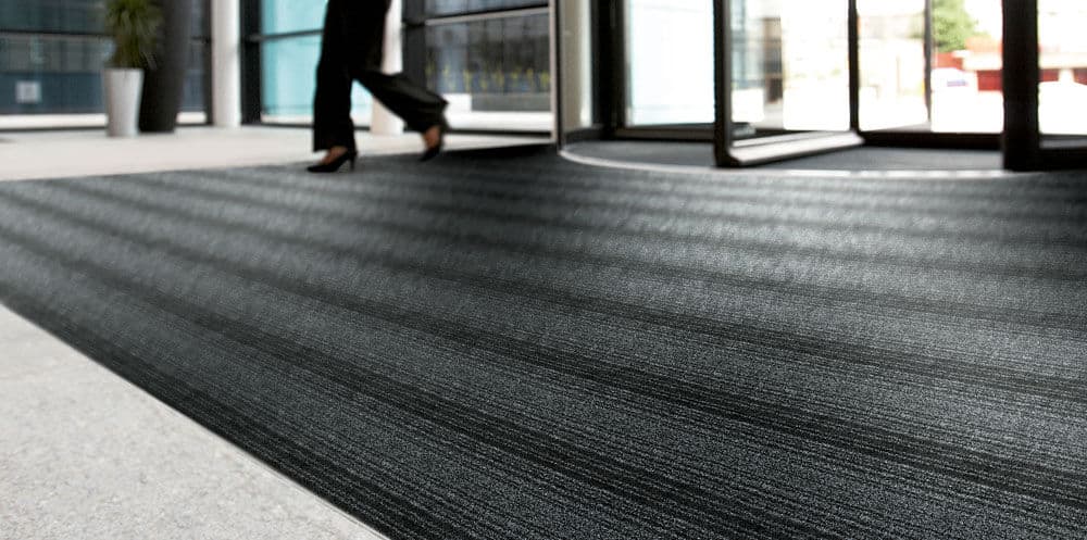 A person walking down a hallway with a black **business** carpet mat.