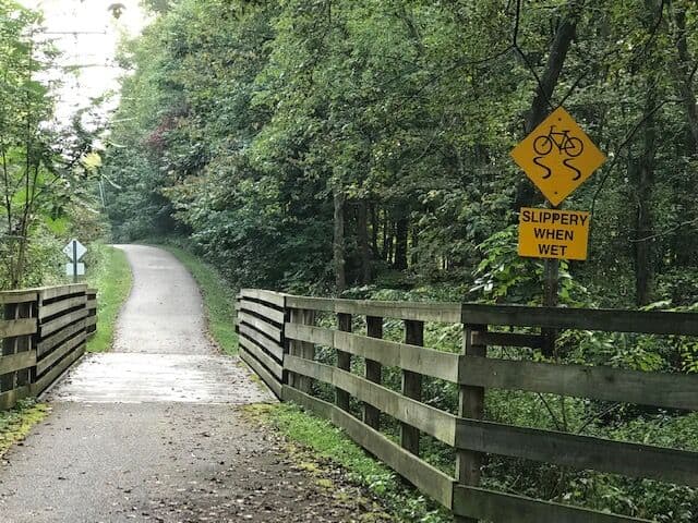 A wooden bridge in the woods with a sign on it promoting safety.