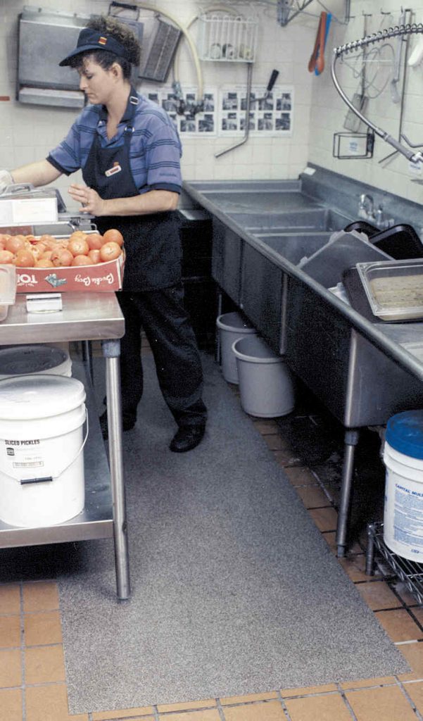 A woman is cooking in a kitchen to reduce slips and falls in the workplace.