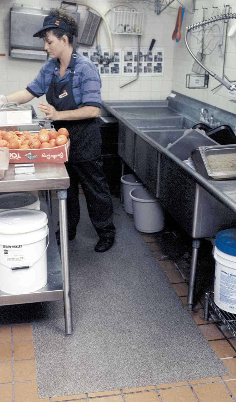 A woman is cooking in a kitchen to reduce slips and falls in the workplace.