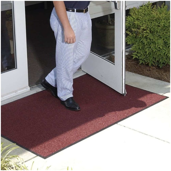 A man standing in front of a door with a doormat made of Brush Hog Floor Mat material.