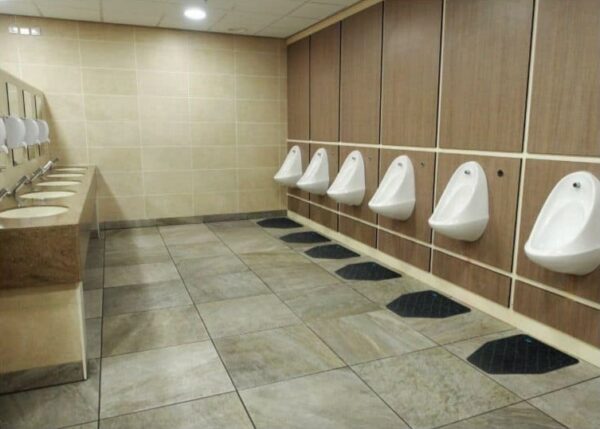 A clean men's restroom with urinals and sinks features a CleanShield™ Urinal Floor Mat.