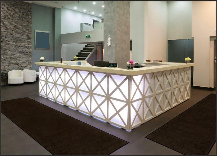 The reception area of a hotel with a white counter and Plush Floor Mat.