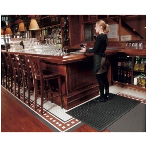 A woman standing on a Comfort Flow Floor Mat in front of a bar.