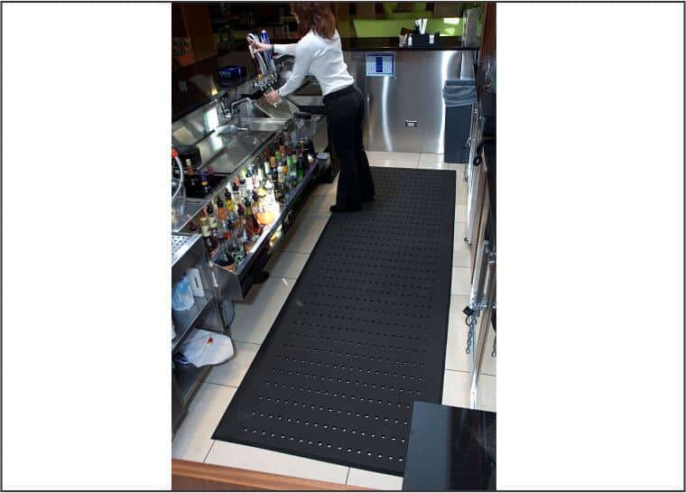 A woman standing in front of a bar on a Complete Comfort Floor Mat for complete comfort.
