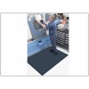 A man operates a machine in a factory while standing on a Complete Comfort Floor Mat.