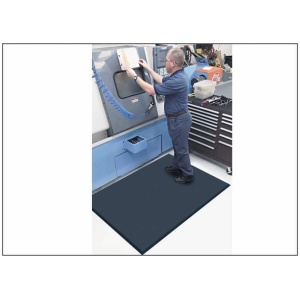 A man operates a machine in a factory while standing on a Complete Comfort Floor Mat.