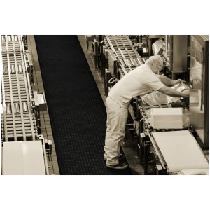 A man on a Cushion Station Floor Mat working on a conveyor belt in a factory.