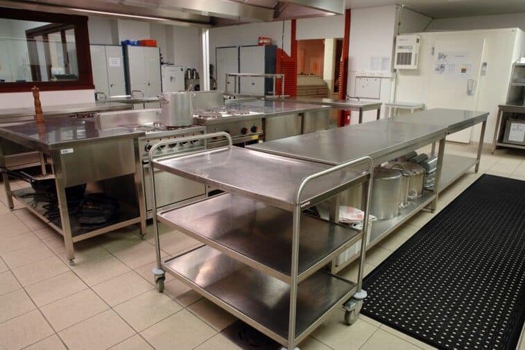 A commercial kitchen with stainless steel counter tops and a Cushion Station Floor Mat.