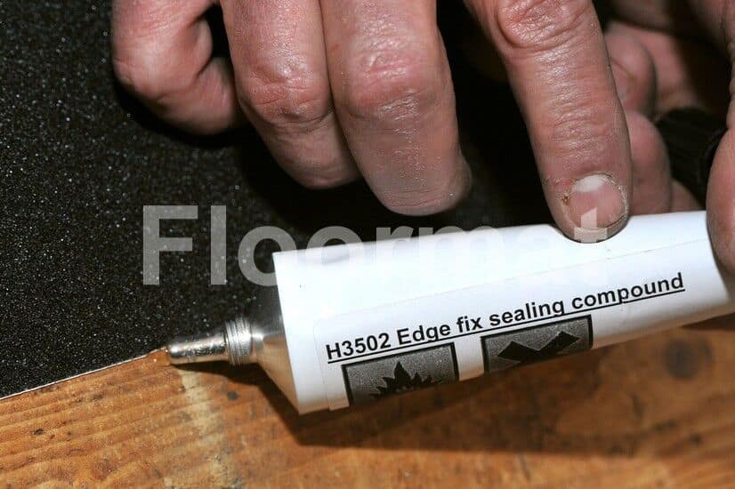 A person applying Floormat Edge Fix Sealing Compound on a wooden floor.