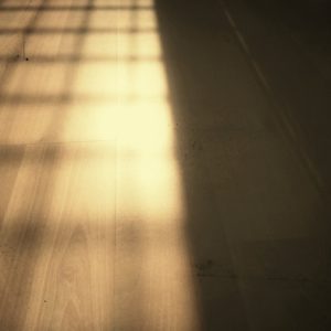 A wooden floor with a light shining through the bars, highlighting the dangers of cheap floor mats.