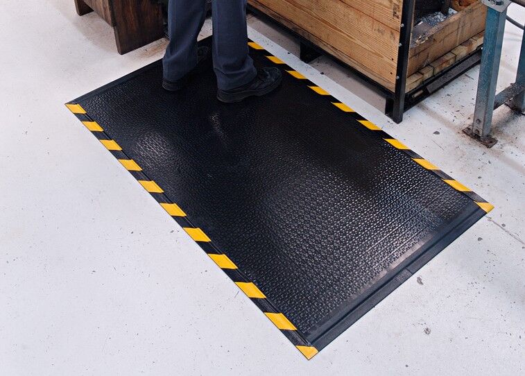 A person standing on a DuraComfort Textured Floor Mat in a warehouse.