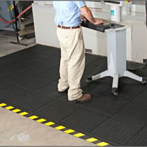 A man operating a machine in a factory, with the assistance of a safety mat for workplace safety.