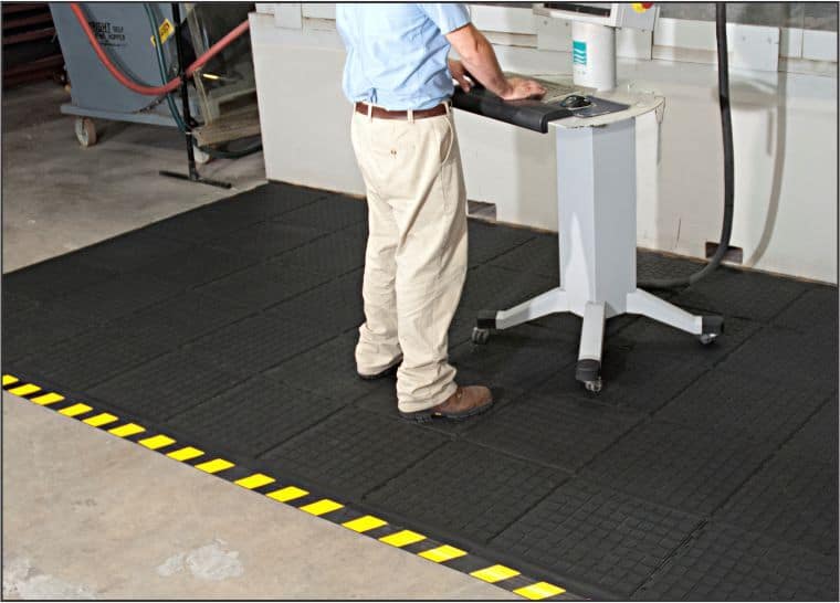 A man operating a machine in a factory, with the assistance of a safety mat for workplace safety.