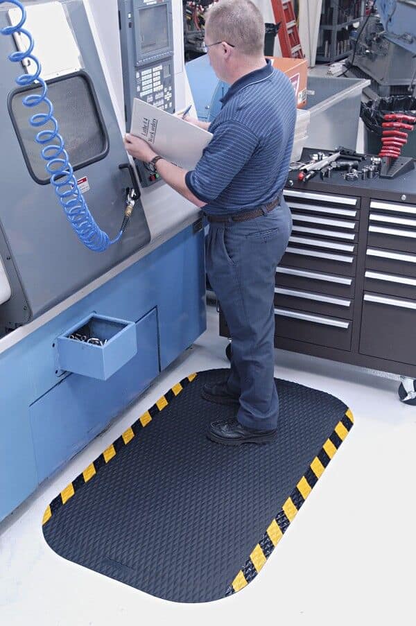 A man operating a machine in a factory, utilizing industrial mats for safety and productivity.
