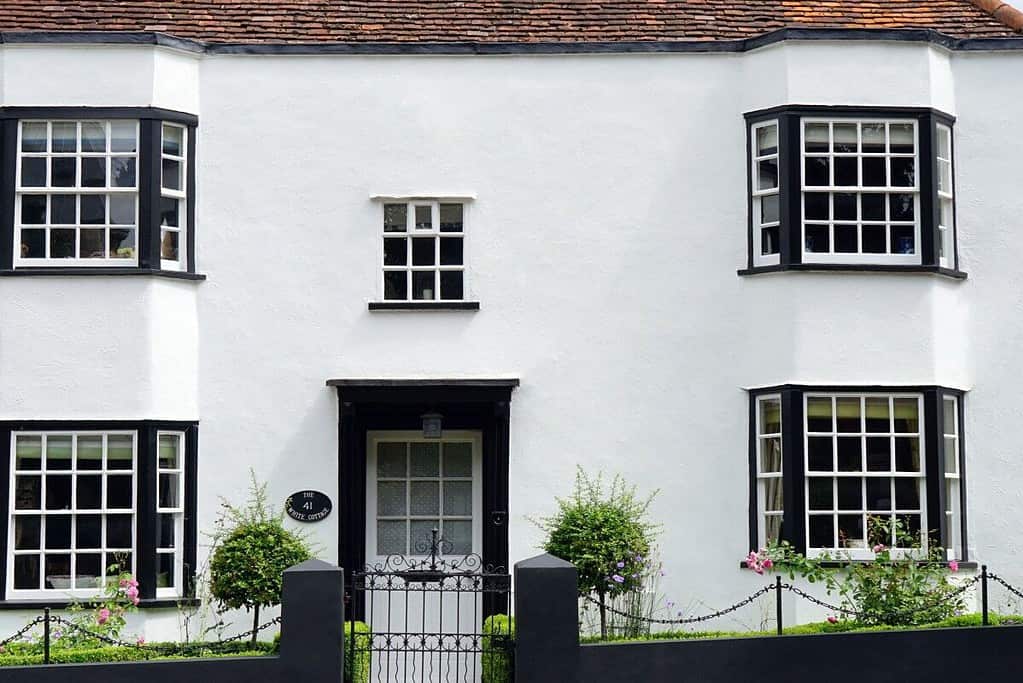 A white house with black shutters and a black fence featuring floor mats.