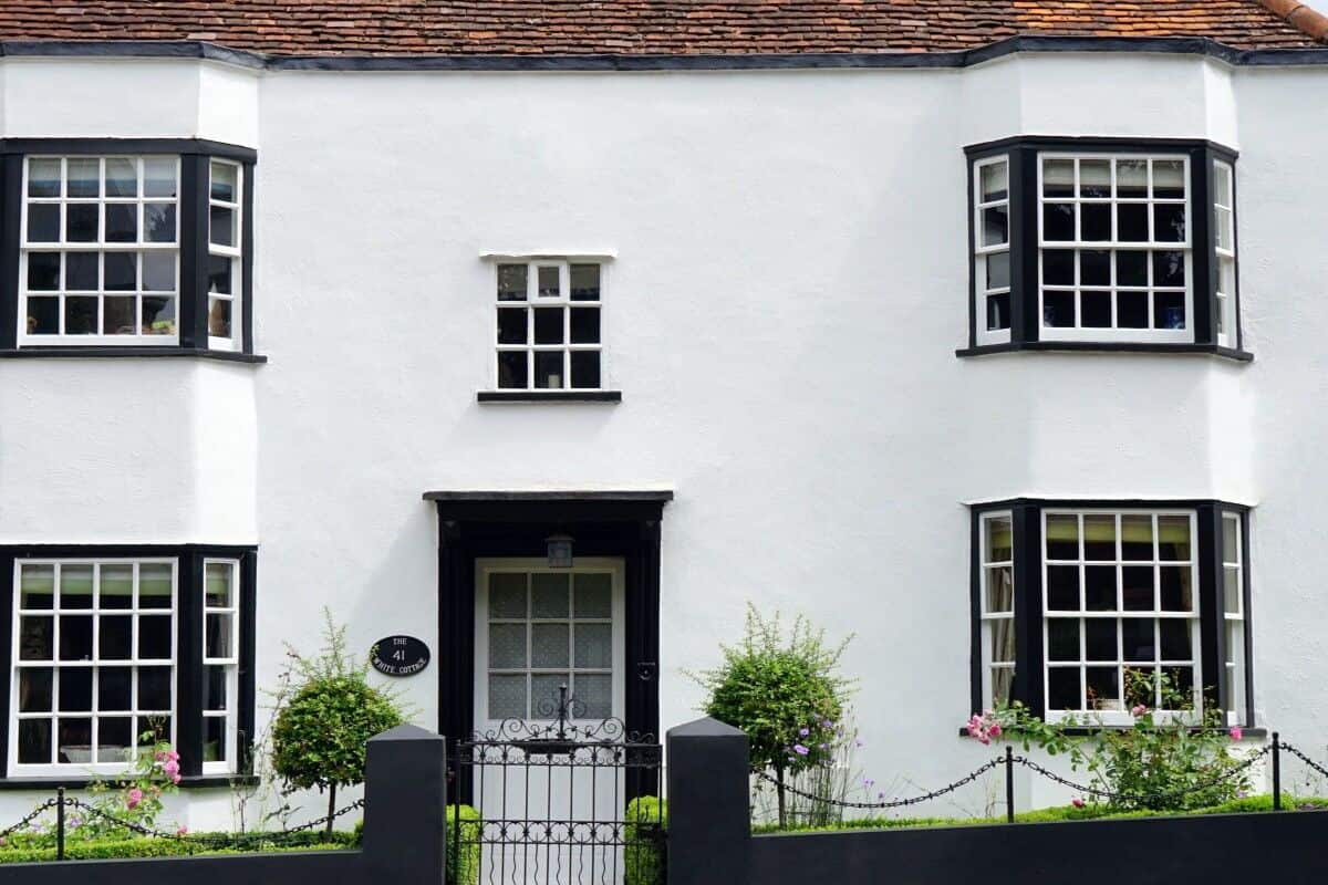 A white house with black shutters and a black fence featuring floor mats.