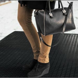 A woman is holding a black handbag in the snow using a heated mat.