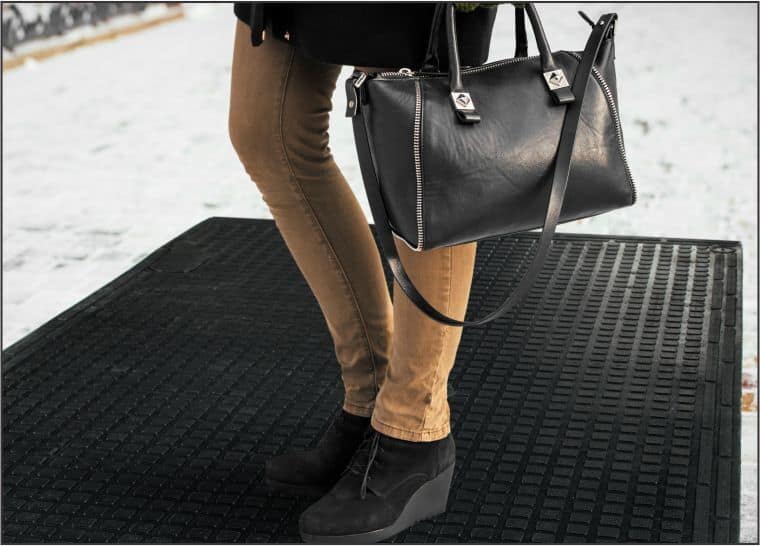 A woman is holding a black handbag in the snow using a heated mat.