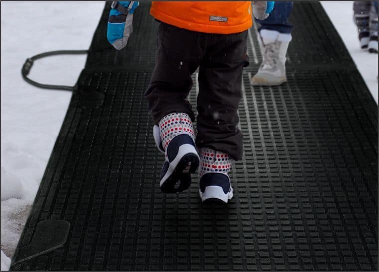 Two children walking on a Melt Step Snow Melting Mat in the snow before it starts to melt.