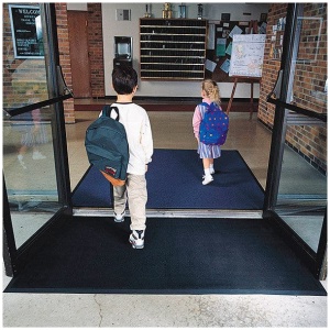 Two children with backpacks entering a doorway while holding a Rubber Brush.