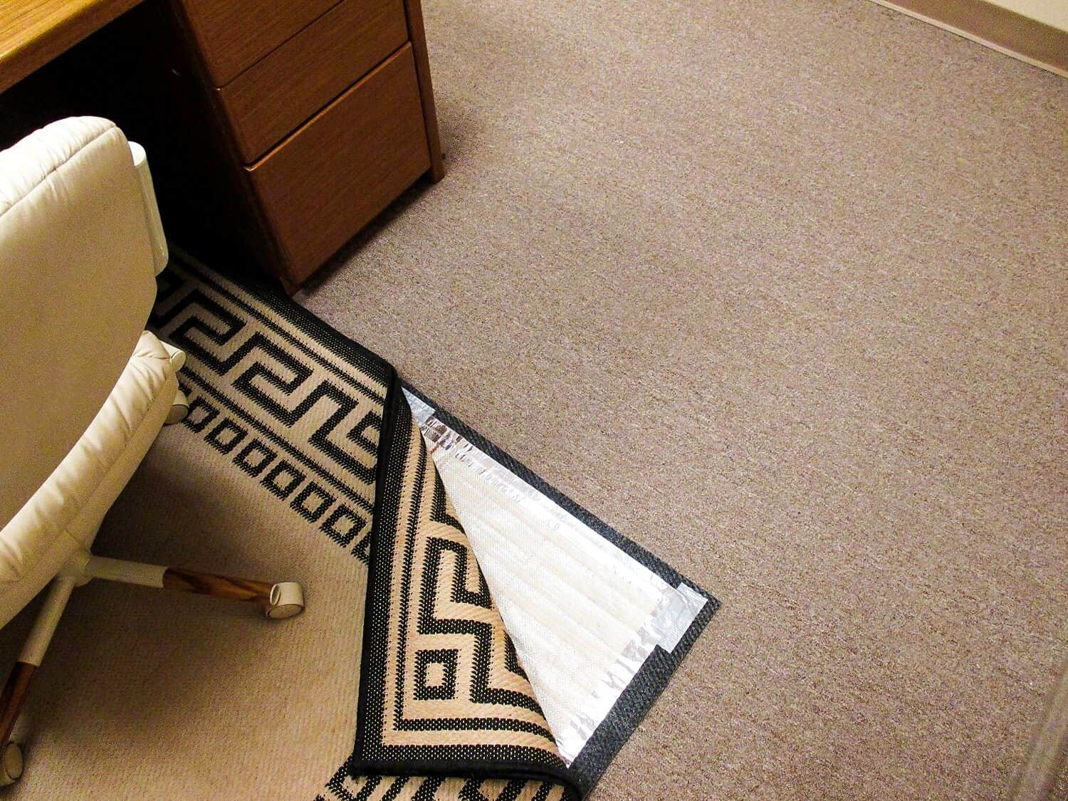 A desk with a RugBuddy Under Rug Heating Panel next to it.