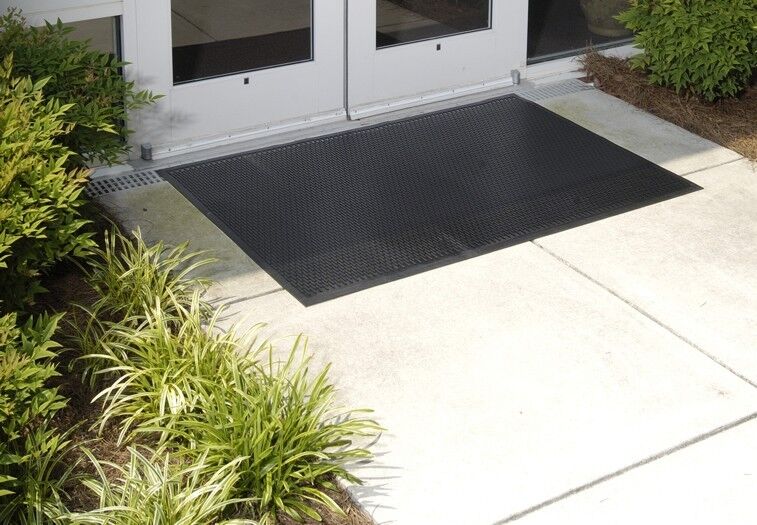 A Super Scrape Floor Mat is placed in front of a door.