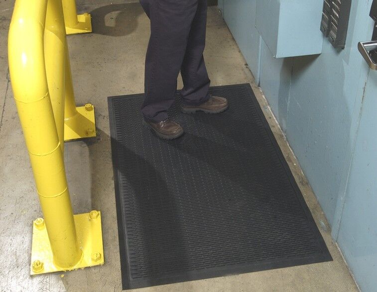 A man standing on a Super Scrape Floor Mat in a factory.