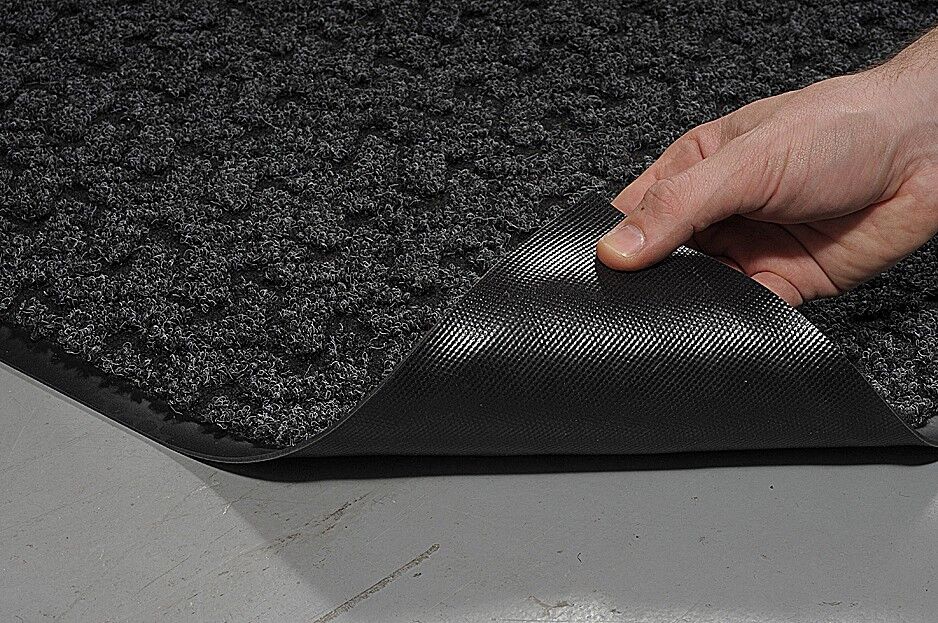 A person placing a black mat on a floor.