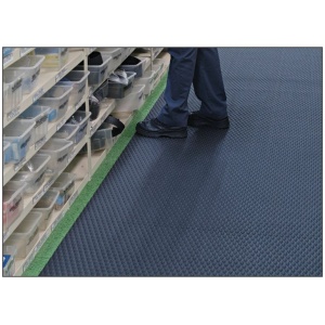 A person standing on a Traction Tread Floor Mat in a warehouse.