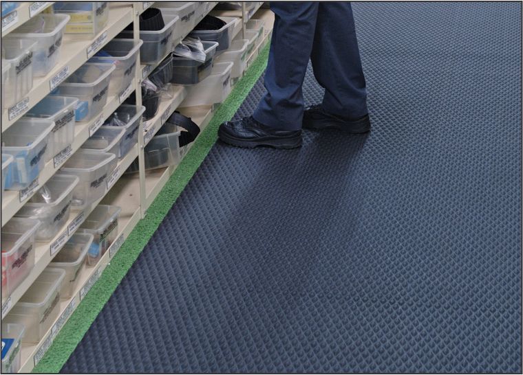 A person standing on a Traction Tread Floor Mat in a warehouse.