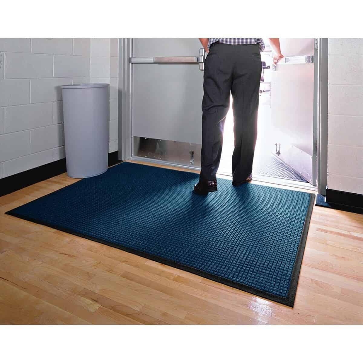 A man standing in front of a door with a WaterHog Classic Floor Mat.