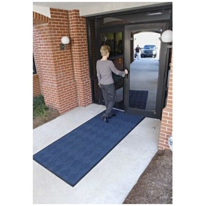 A woman walking into a building with a WaterHog Eco Premier Floor Mat.