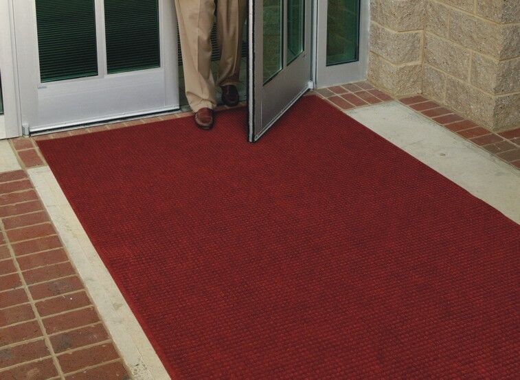 A man standing at the door of a building, with a WaterHog Fashion Floor Mat.
