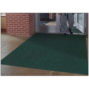 A person is standing in front of a door with a green WaterHog Fashion Floor Mat.