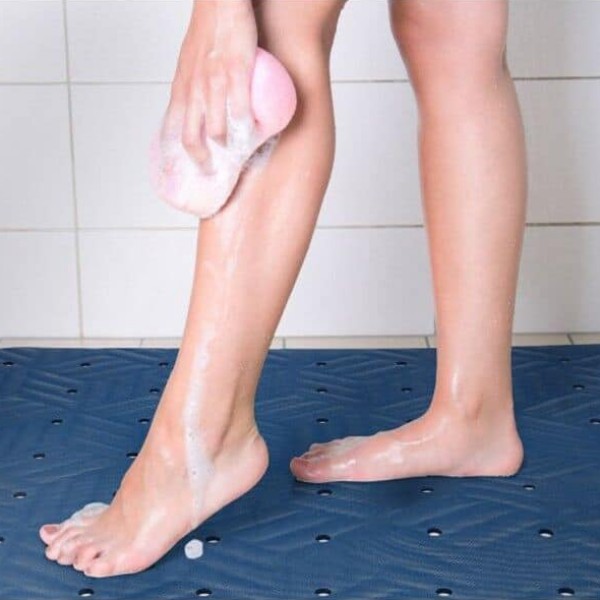 The woman carefully washes her legs, using a sponge on the Wet Step Floor Mat for stability.