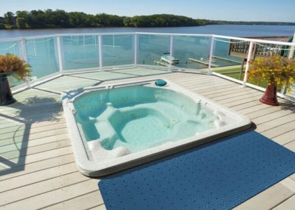 A hot tub on a deck overlooking a lake, with the added convenience and safety of the Wet Step Floor Mat.